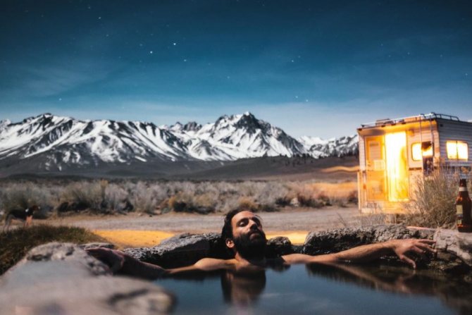 Мужчина с бородой, лежащий в ванне из камней на фоне гор